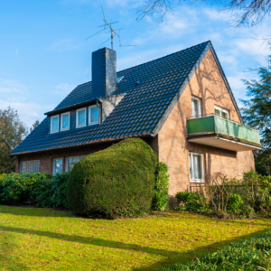 Eine Immobilie von der Seite fotografiert. Ein Haus mit Schornstein und einem grünen gepflegten Garten